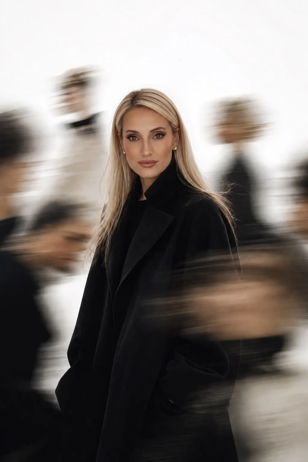 Bruna Malucelli de casaco preto, parada e nítida, com pessoas passando desfocadas ao redor